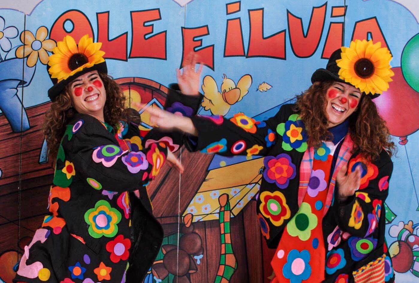 Ole e Ilvia in costume da pagliacce ridono davanti al cartellone