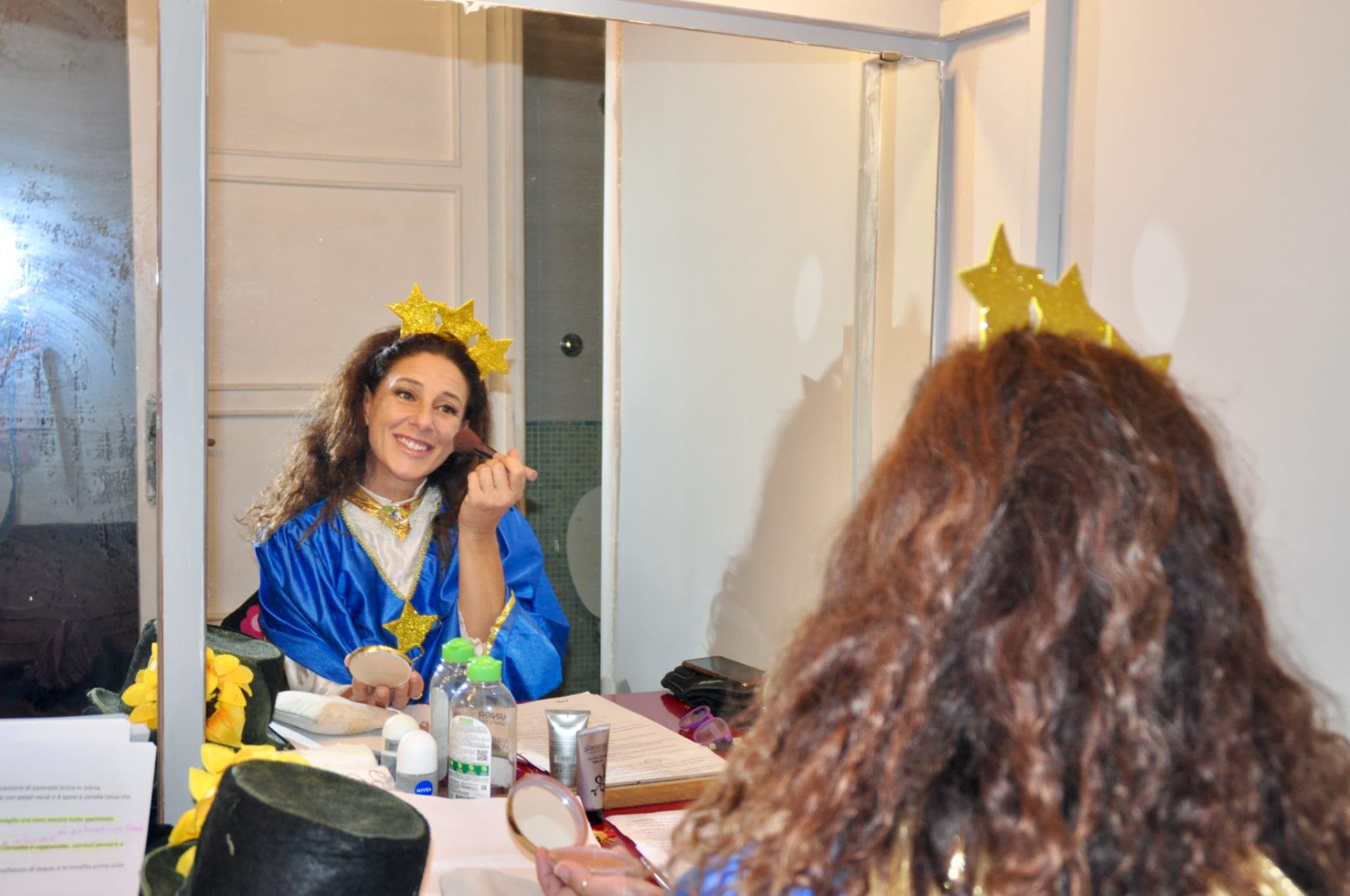 Artista con corona di stelle si trucca allo specchio in camerino